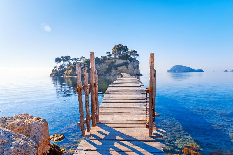 Ein Steg im Familienurlaub Zakynthos mit klarem stillen Meer und kleinen Inseln bei Sonnenschein