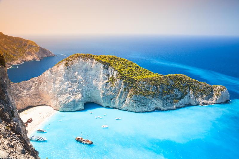 Aussicht auf eine Bucht mit weißem Strand, türkisen Meer, Booten und Felsformationen im Familienurlaub Zakynthos