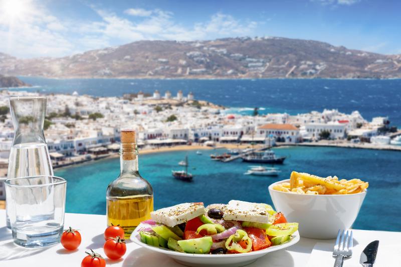 Ein Tisch mit traditionellen griechischen Speisen und eine Aussicht auf das Meer im Familienurlaub Griechenland günstig