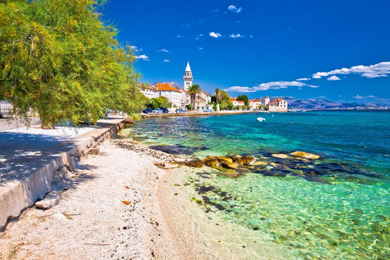Strand mit türkisblauen Meer und Stadt im Hintergrund im Familienurlaub Kroatien günstig.