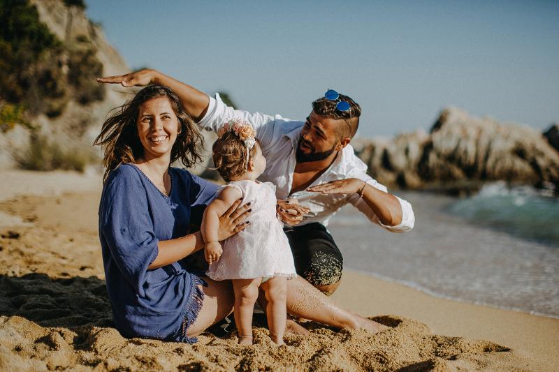 Eine Familie spielt am Strand, das Kind steht im Sand zwischen den Eltern
