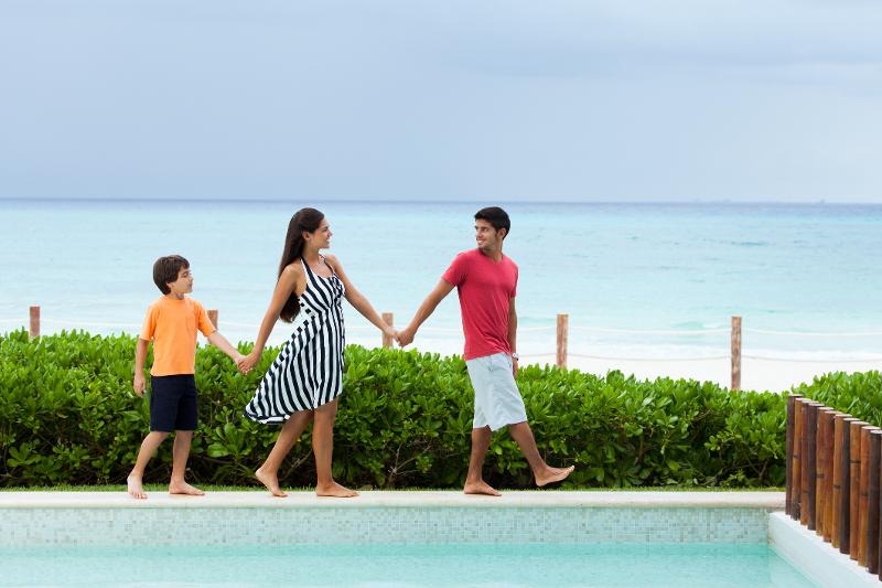 Eine Familie spaziert Hand in Hand am Pool entlang mit dem Meer im Hintergrund.