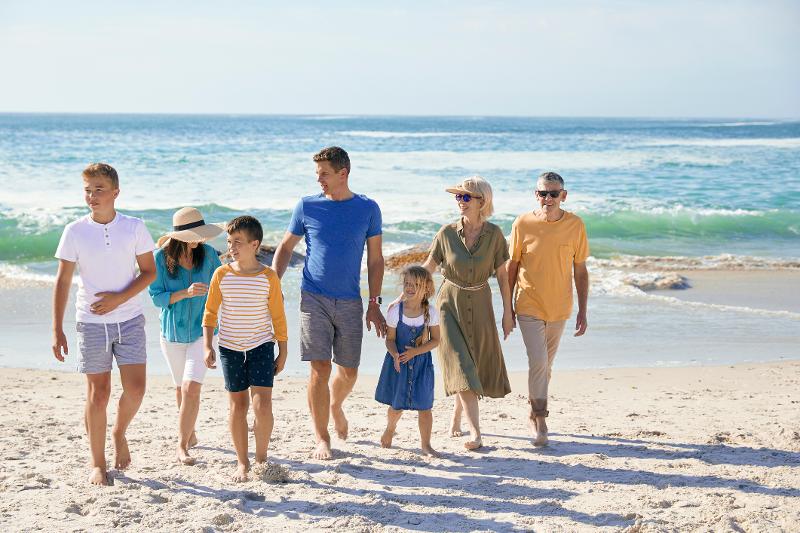 Drei Kinder, ihre Eltern und Großeltern laufen gemeinsam lachend am Strand entlang