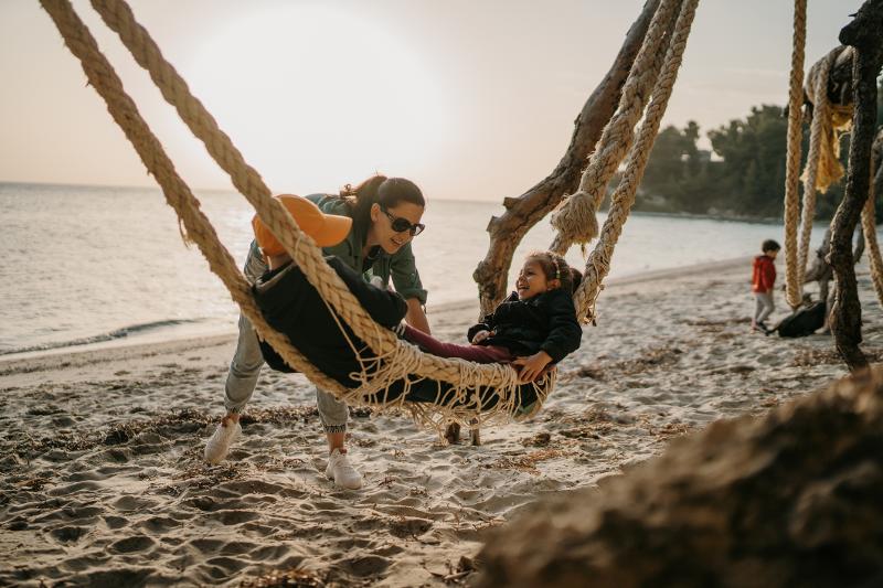 Mutter schaukelt Kindern in einer Hängematte am Strand im Herbsturlaub mit Kindern
