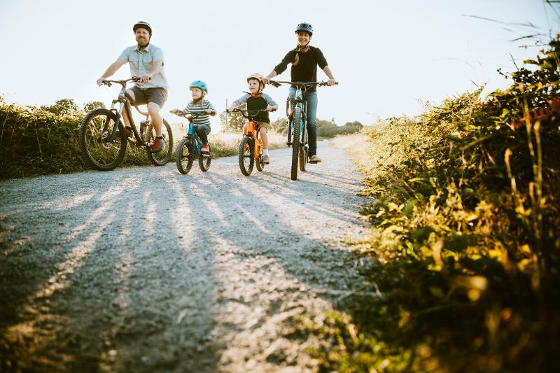 Eine Familie fährt gemeinsam Fahrrad auf einem sonnigen Pfad im Kinderurlaub