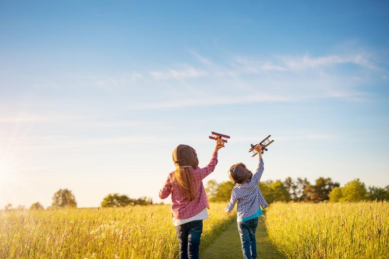Zwei Kinder spielen mit Spielzeugflugzeugen auf einem Feld bei Sonnenuntergang.