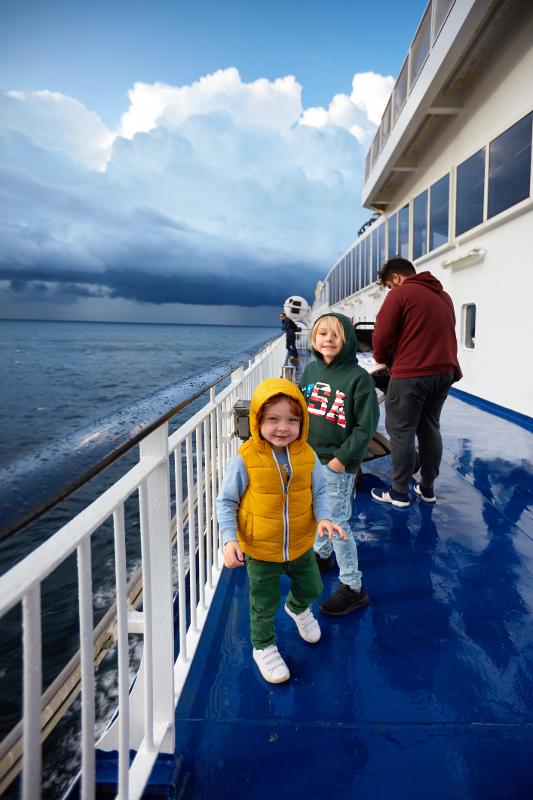Zwei Kinder mit Kapuzenjacken auf dem Deck eines Kreuzfahrtschiffes mit stürmischen Wolken im Hintergrund