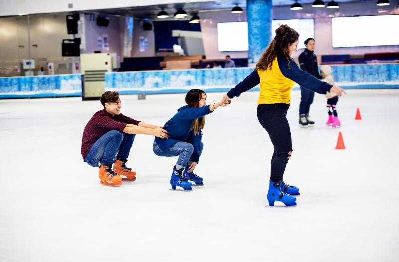 Drei Menschen, die im Kurztrip Berlin mit Kindern in einer Halle eislaufen und sich aneinander festhalten