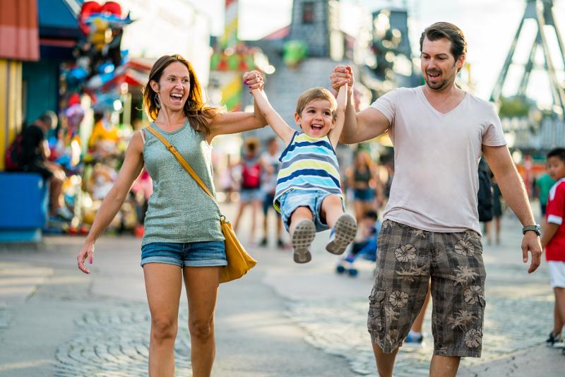 Eine Familie, die im Kurztrip Berlin mit Kindern auf einem Jahrmarkt spaziert und ihren Sohn an den Händen hält