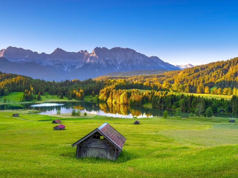 Der Geroldsee im Kurzurlaub mit Kindern Bayern mit Holzhäusern auf einer grünen Wiese und vielen Bäumen und Bergen im Hintergrund