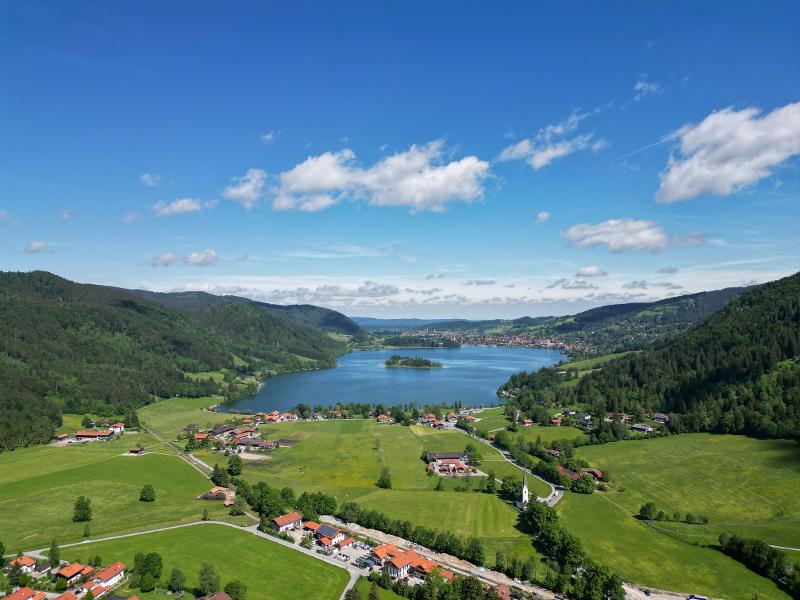 Aussicht auf einen See mit kleiner Insel und Häusern, einer Wiese und einer bergigen Waldlandschaft im Kurzurlaub mit Kindern Bayern