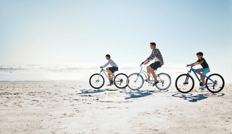 Ein Vater und zwei Kinder, die im Kurzurlaub mit Kindern Deutschland Fahrrad am Strand fahren