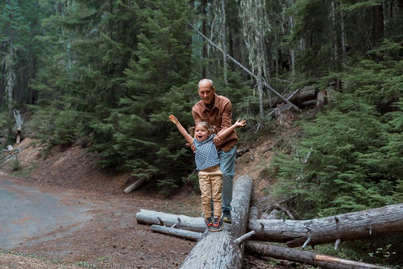 Ein Großvater und ein Kind, die im Kurzurlaub mit Kindern Deutschland auf einem umgefallenen Baum balancieren