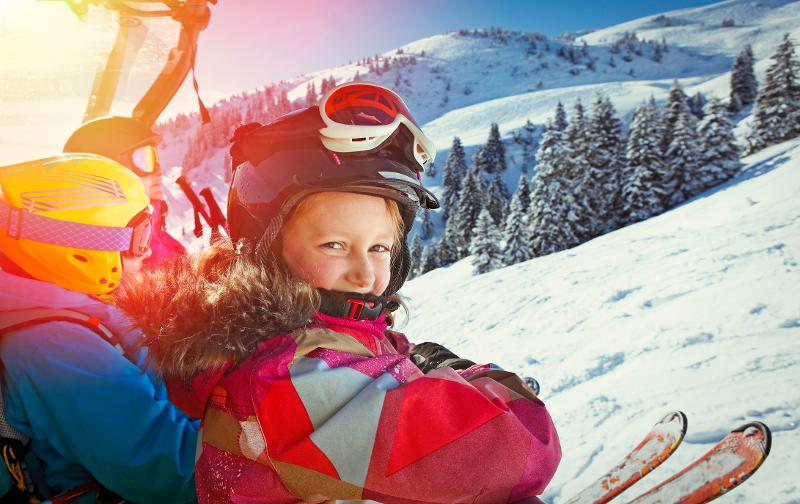 Ein Kind, welches im Kurzurlaub mit Kindern Deutschland auf einem Skilift sitzt und in die Kamera lächelt. Im Hintergrund erkennt man Schnee und Bäume