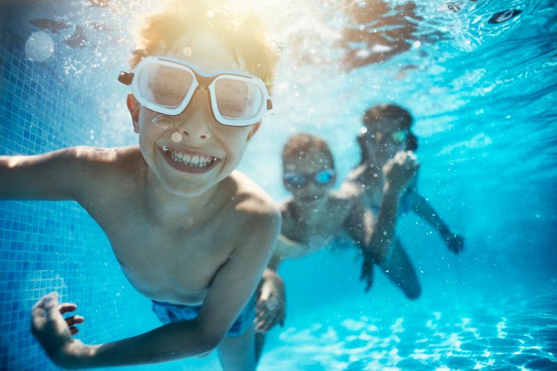 Drei Kinder, die im Kurzurlaub mit Kindern in einem Pool tauchen und mit Taucherbrille in die Kamera lachen