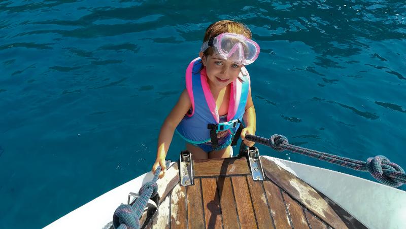Ein Mädchen trägt eine Schwimmweste und Taucherbrille und steigt auf ein Boot im Mallorca Urlaub mit Kindern günstig