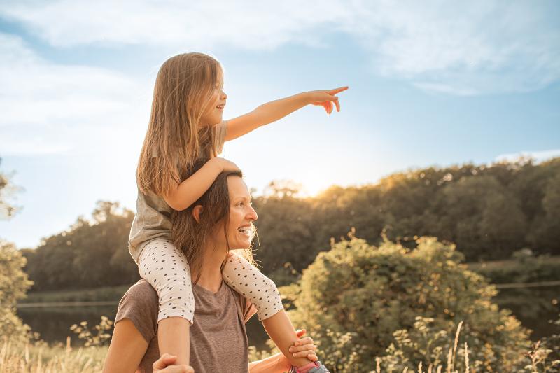 Eine Mama trägt ihr Kind auf Pauschalreise Familie Mallorca auf den Schultern