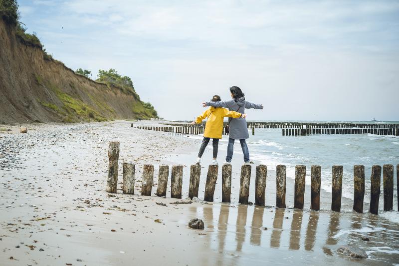 Kinder und Erwachsene balancieren auf Holzpfählen am Strand.