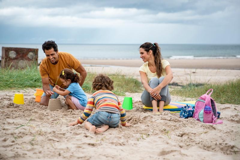 Familie sitzt im Sand und spielt