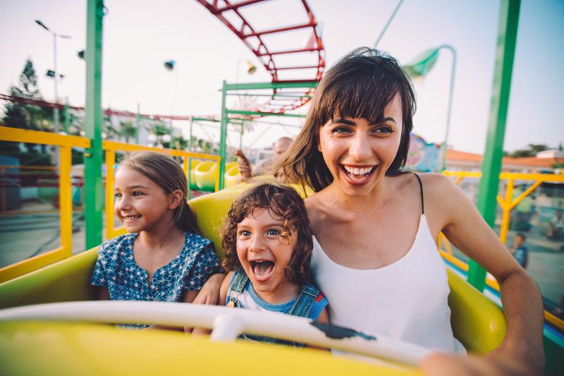 Eine glückliche Mutter auf der Reise mit Kindern fährt mit ihren zwei fröhlichen Kindern auf einer Achterbahn.