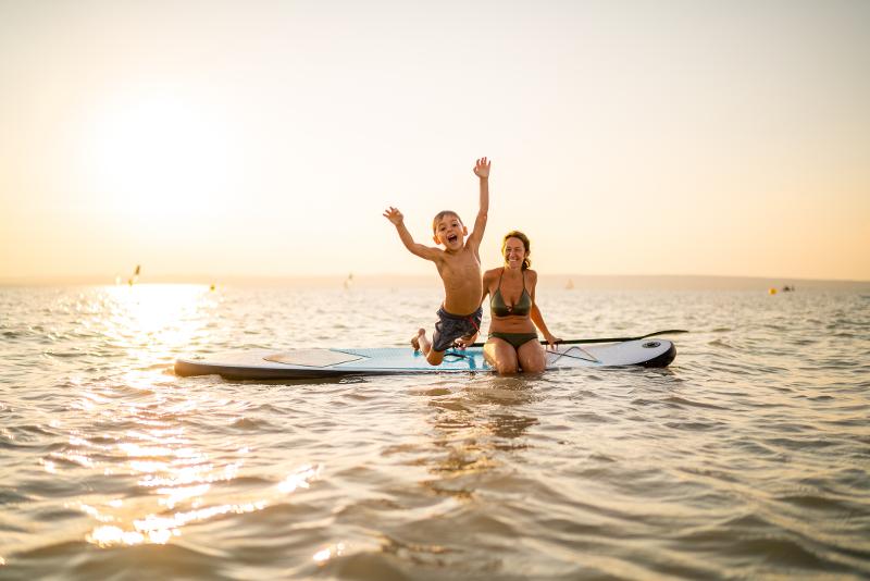 Eine Reise mit Kindern, in der eine Mutter und ihr Kind, zusammen auf einem Surfbrett im Meer spielen und Spaß haben