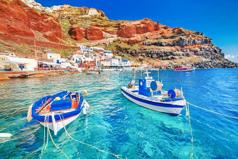 Zwei Boote auf dem Meer und eine Ortschaft und Felsen im Santorini Urlaub mit Kindern