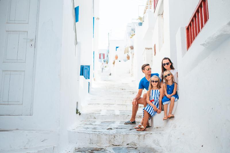 Eine Familie, die auf Treppen in einer Weißen Gasse mit blauen Fenster Lehnen im Santorini Urlaub mit Kindern sitzt