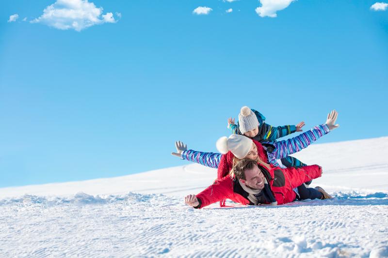 Eltern und Kind toben im Schnee im Skiurlaub Österreich mit Kindern