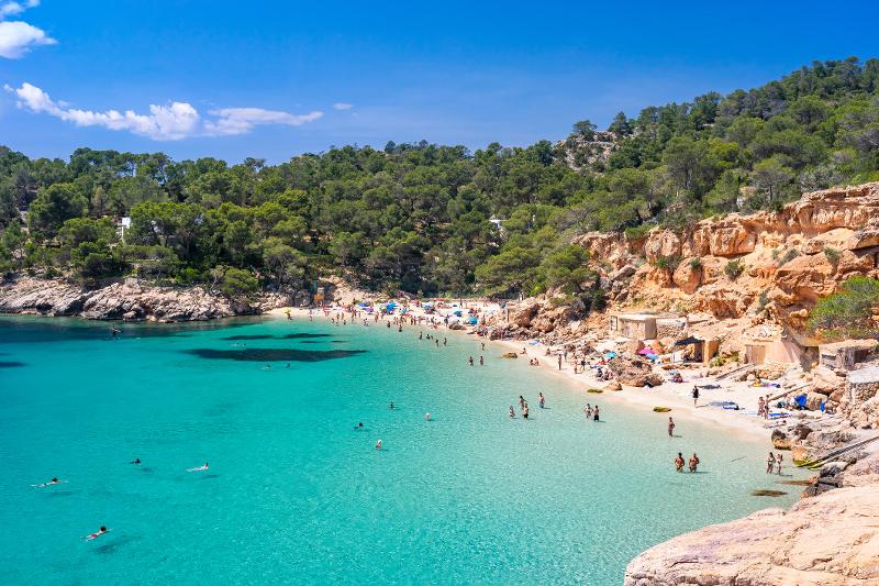 Sicht auf eine Bucht mit hellblauem Meer, weißen Strand und Menschen im Spanien Urlaub mit Kindern All Inclusive