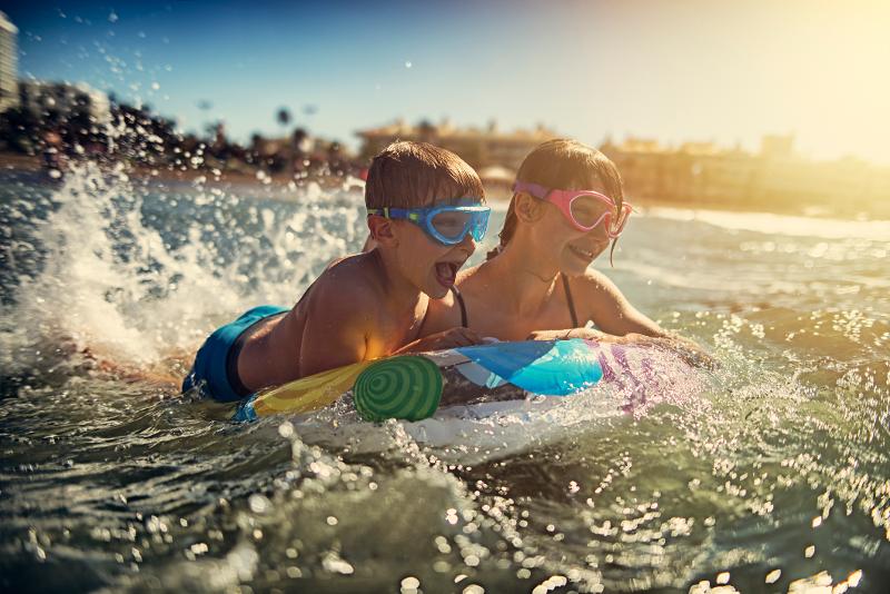 Zwei Kindern, die mit Taucherbrille und Schwimmreifen im Meer planschen und im Spanien Urlaub mit Kindern am Meer Spaß haben