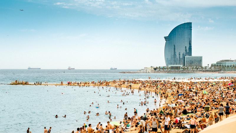 Ein Strand am Meer in Barcelona mit Menschenmassen und Hochhaus im Spanien Urlaub mit Kindern am Meer
