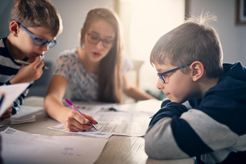 Kinder sitzen auf einer Familiensprachreise zusammen an einem Tisch und bearbeiten Lernzettel
