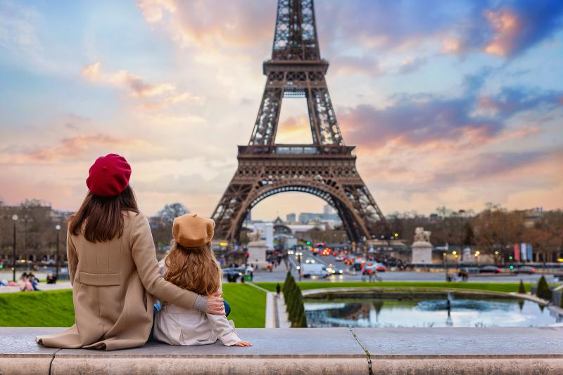  Mutter und Kind sitzen im Sonnenuntergang vor dem Eiffelturm beim Städtetrip mit Kindern