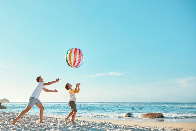 Zwei Kinder spielen am Strand mit einem großen, bunten Wasserball