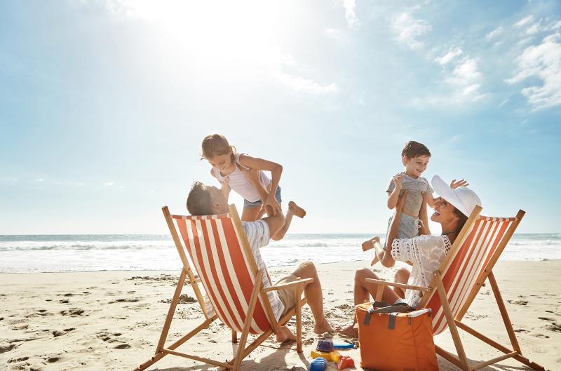 Zwei Strandliegen am Wasser, Mutter und Vater werfen sitzend die Kinder in die Luft