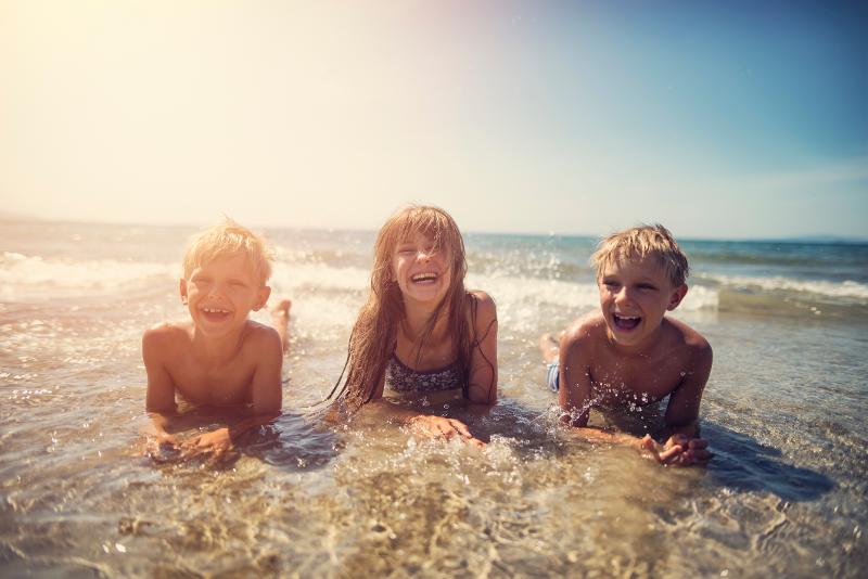 Drei Kinder liegen im Urlaub günstig mit Kindern in Deutschland in der Brandung des Meeres am Strand