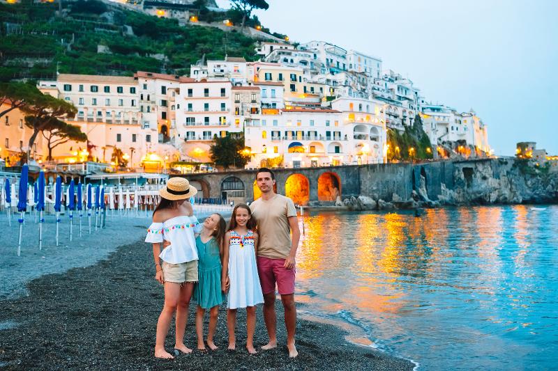  Eine glückliche Familie steht am Strand und genießt den Abend im Urlaub in Italien mit Kindern und Auto