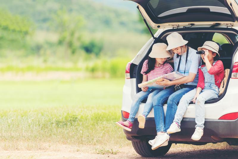 Eine Familie sitzt gemeinsam im Kofferraum eines Autos mit Fernglas und Karte