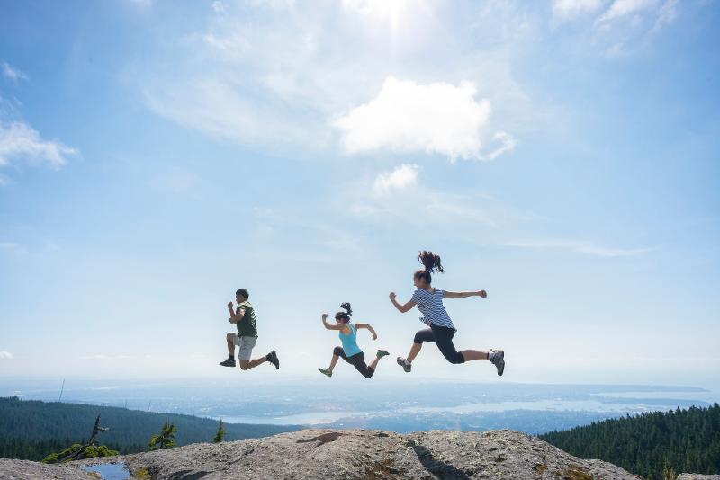 Mutter und zwei Kinder springen vor einer Bergkulisse in die Luft