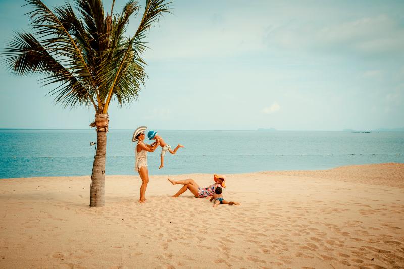 Familie genießt ihren Urlaub mit Kindern All Inclusive am Strand mit einer Palme.