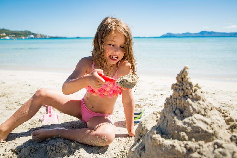 Mädchen buddelt am Sandstrand im Urlaub mit Kindern Balearen