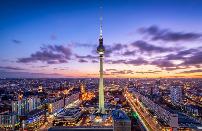 Der Berliner Fernsehturm bei Sonnenuntergang, umgeben von den hell erleuchteten Straßen und Gebäuden der Stadt.