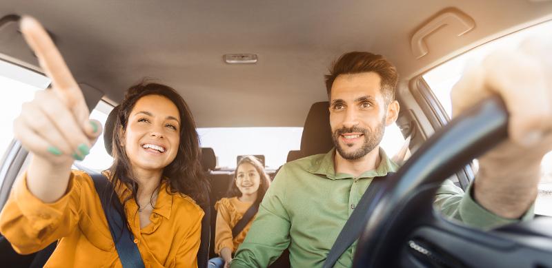  Eltern sitzen mit Kind im Auto und Mutter zeigt nach vorne im Urlaub mit Kindern Frankreich Normandie