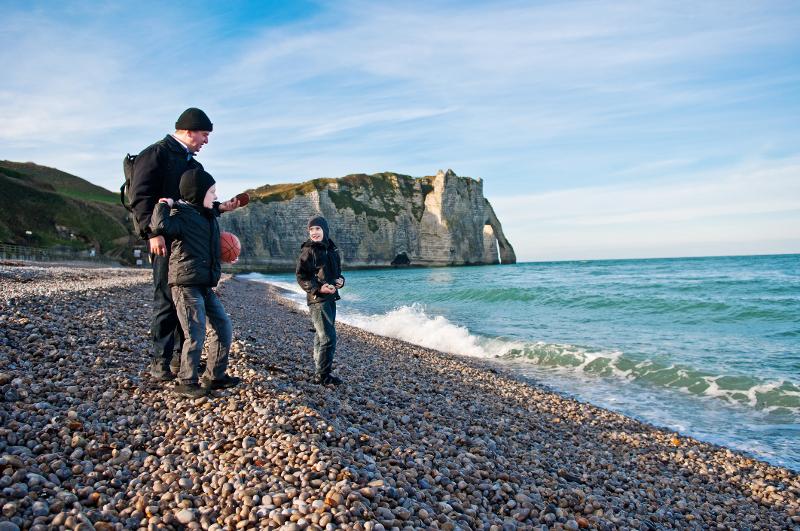  Vater mit zwei Jungs am Steinstrand mit Steilklippe im Hintergrund im Urlaub mit Kindern Frankreich Normandie
