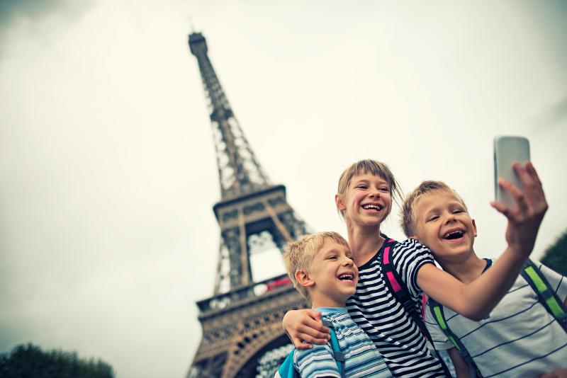 Drei lachende Kinder machen ein Selfie vor dem Eiffelturm in Paris