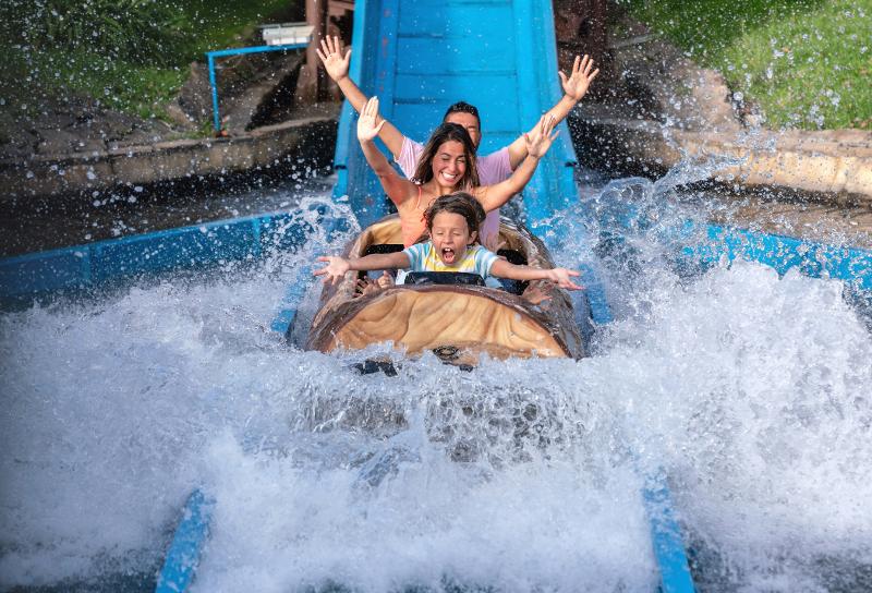 Eine Familie, die im Urlaub mit Kindern Niedersachsen auf einer Wasserrutsche in einem Freizeitpark fährt und die Hände hoch reißt