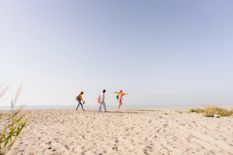 Drei Personen laufen an einem Sandstrand entlang