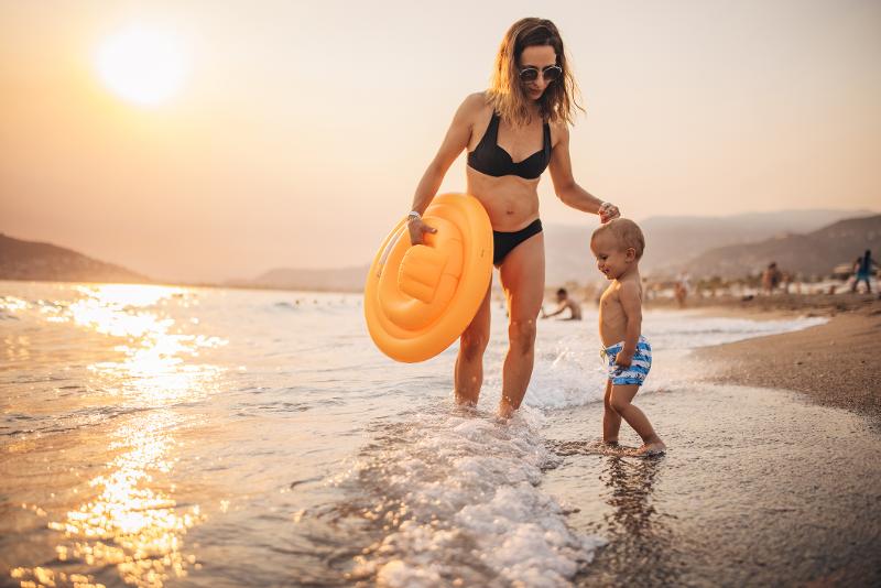 Eine Mutter und ihr Sohn, die im Urlaub mit Kindern Türkei mit einer Luftmatratze am Strand sind und die Füße ins Meer halten
