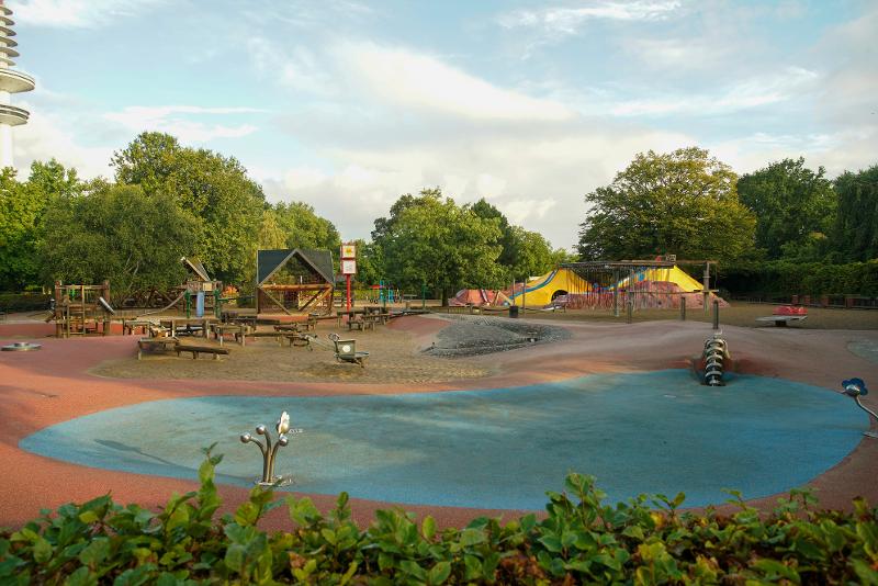 Ein Spielplatz mit verschiedenen Aktivitäten und einem Holzhaus umringt von Bäumen im Wochenende in Hamburg mit Kindern