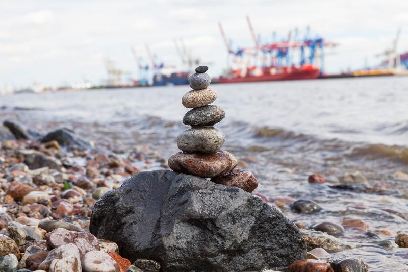 Aufeinander gereihte Steine direkt am Wasser und im Hintergrund der Hafen am Wochenende in Hamburg mit Kindern